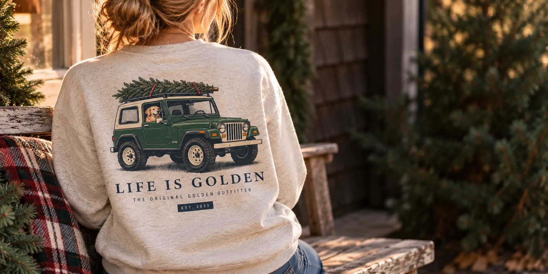 A cream sweatshirt with the Christmas Tree Run dog-and-Jeep artwork on a weathered porch.